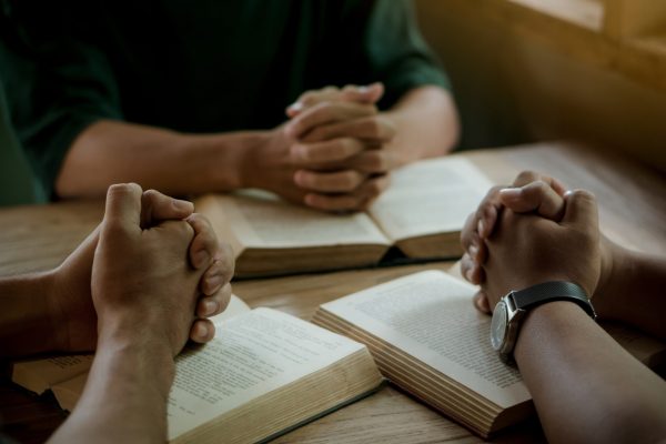 Group of christian people reading and study bible in home and pray together.Group of people holding hands praying worship god.Diverse religious shoot.